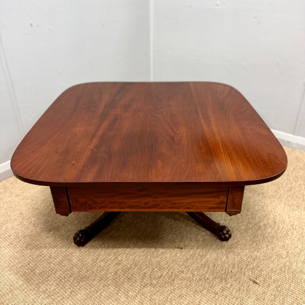 A low English Regency mahogany coffee table with a polished square top, rounded corners, a deep apron, and splayed legs with carved feet.