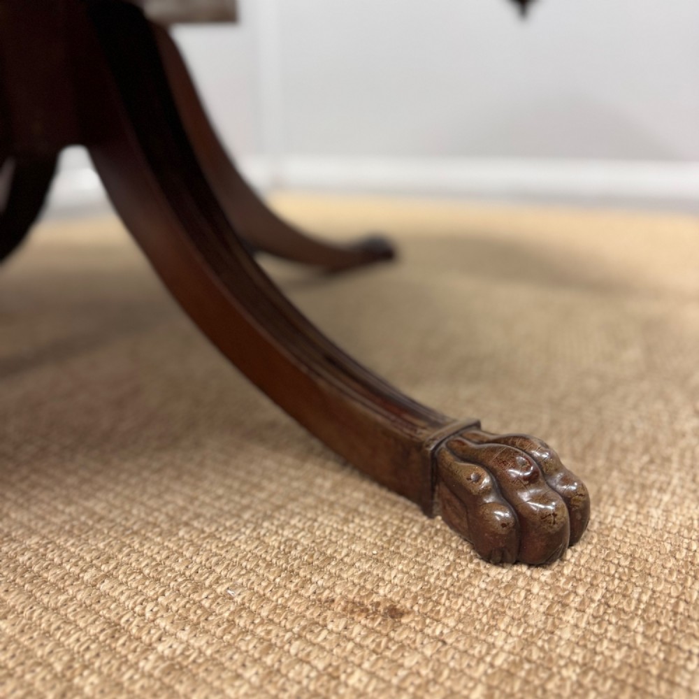 A low English Regency mahogany coffee table with a polished square top, rounded corners, a deep apron, and splayed legs with carved feet. View V