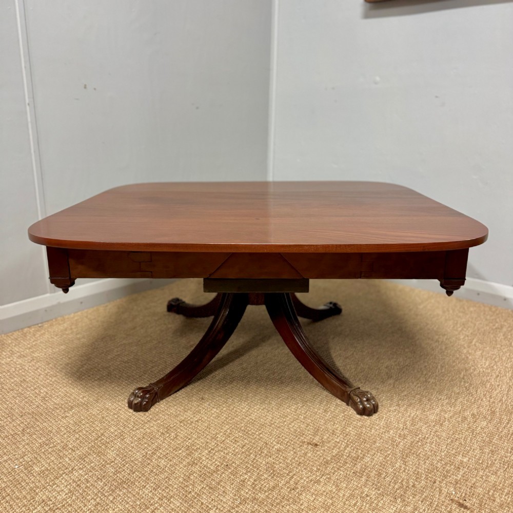 A low English Regency mahogany coffee table with a polished square top, rounded corners, a deep apron, and splayed legs with carved feet. View VI