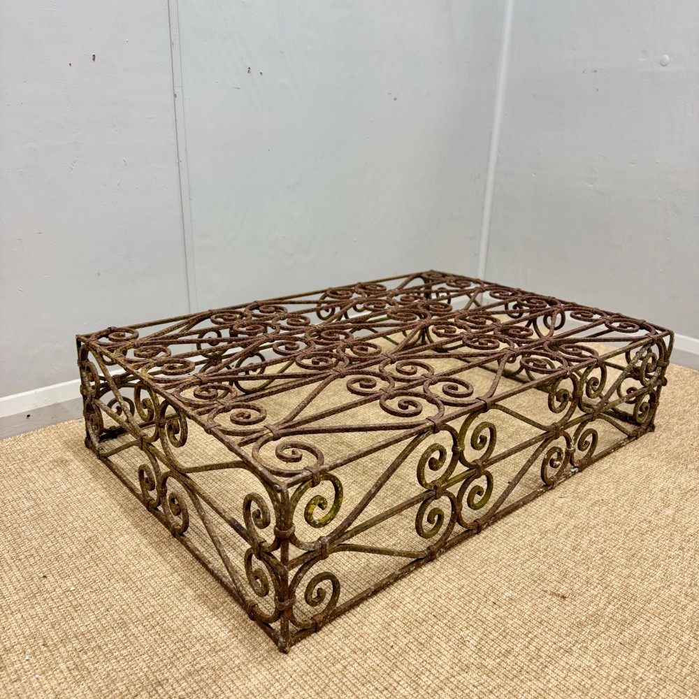 A low rectangular French wrought iron table with ornate C-scroll patterns and a weathered rust finish.