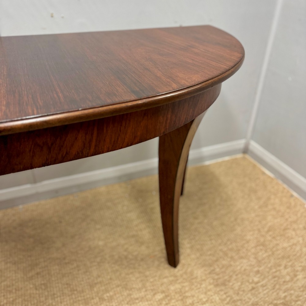 A 19th-century rosewood demilune console table featuring a semi-circular top, plain apron, and four sweeping concave legs. View V