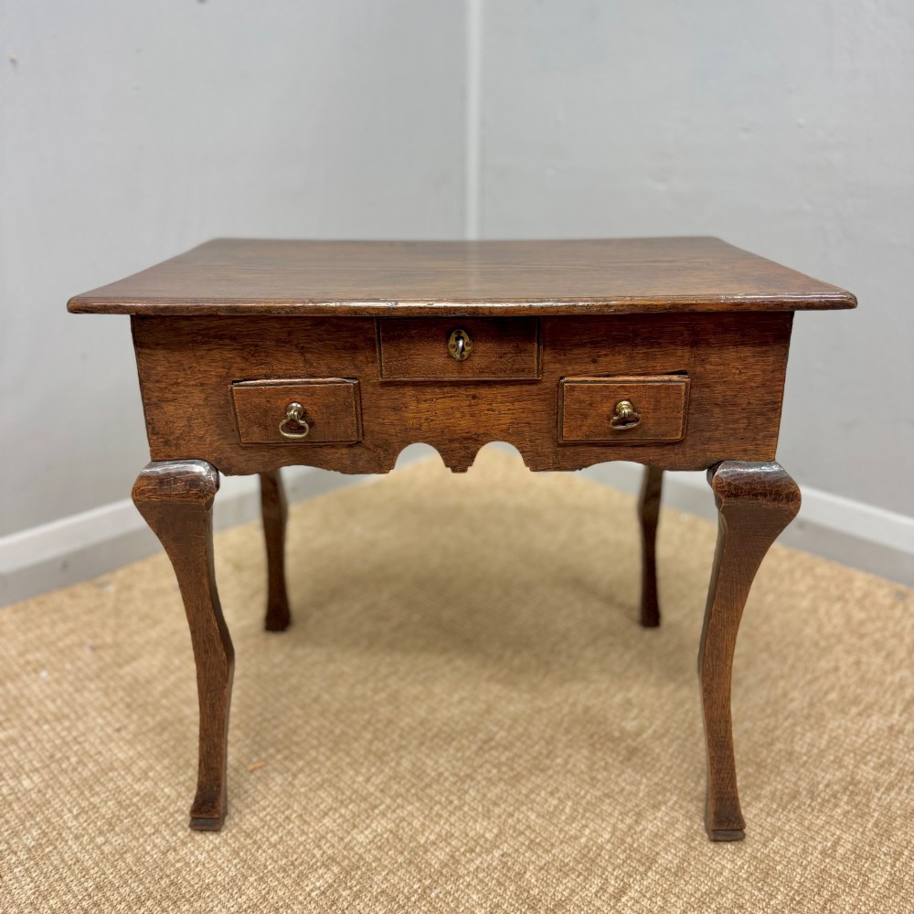 An 18th-century oak low side table featuring cabriole legs, three drawers with brass drop handles, and a shaped apron.