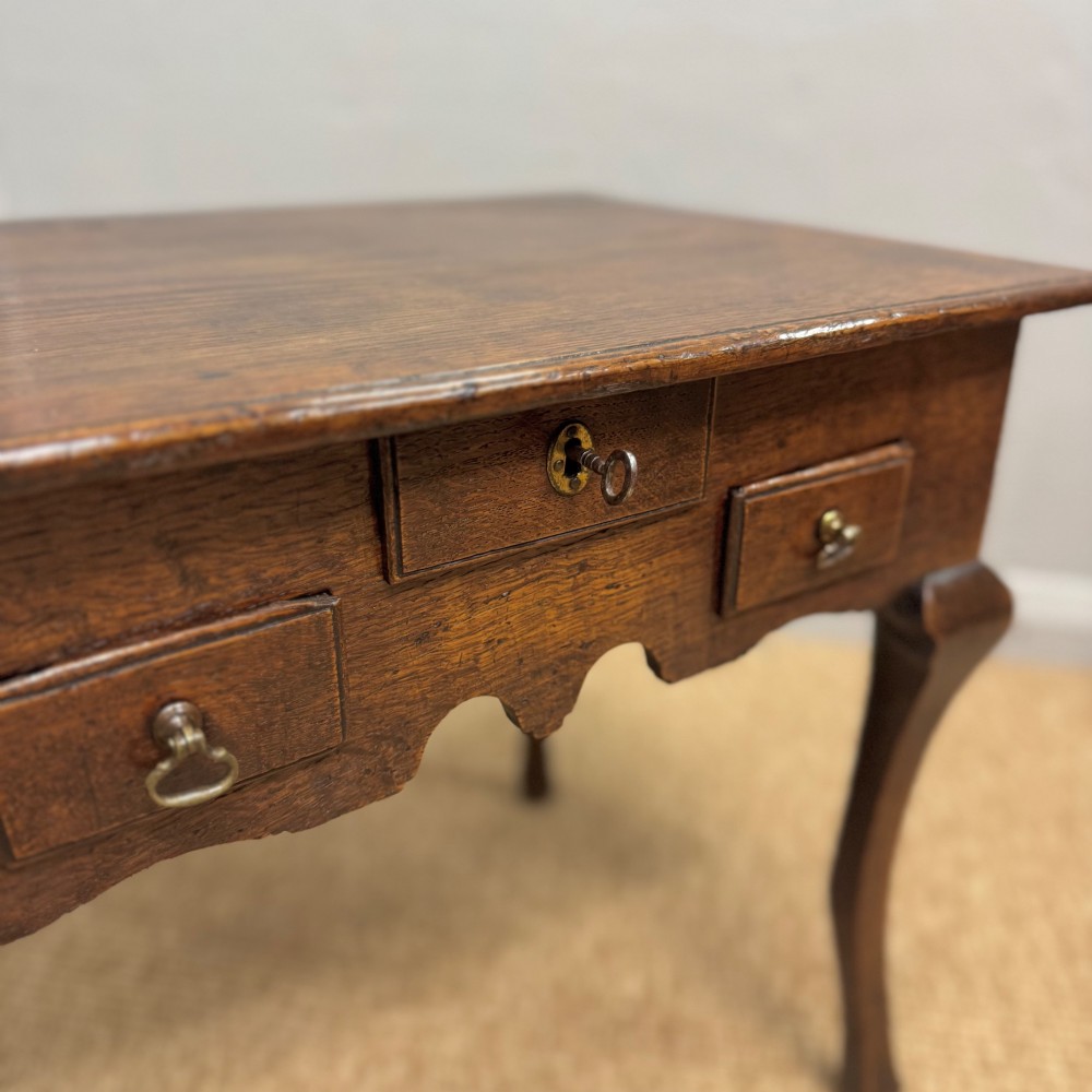 An 18th-century oak low side table featuring cabriole legs, three drawers with brass drop handles, and a shaped apron. View V