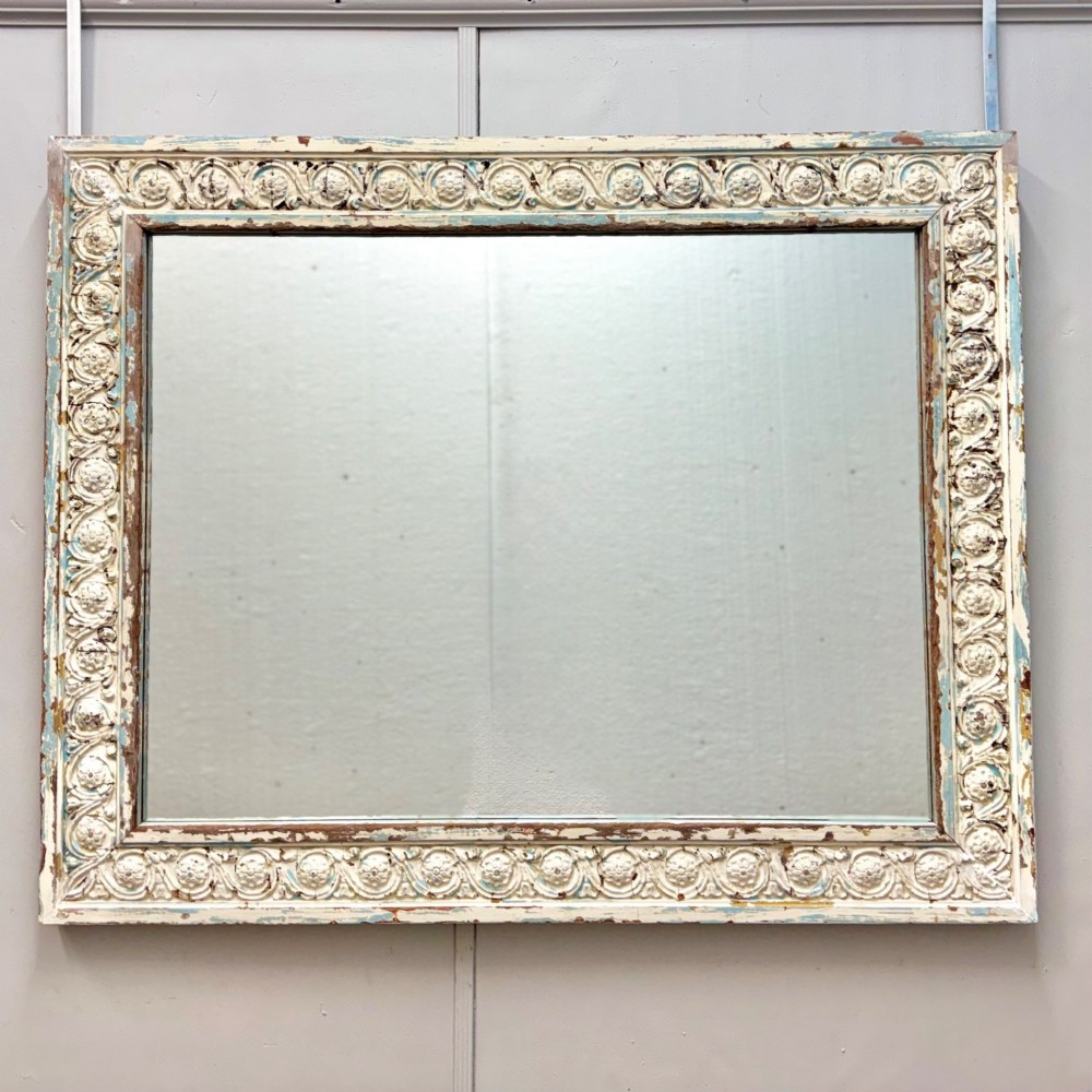 A rectangular 19th-century French overmantel mirror featuring a heavily carved rosette frame with distressed white paint.
