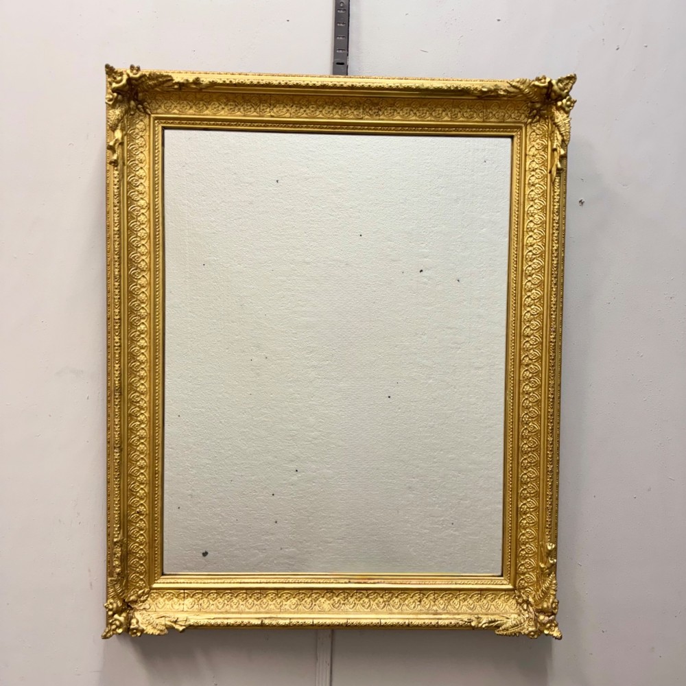 A rectangular nineteenth-century English wall mirror featuring a gold gilded frame with carved foliage corner embellishments and beaded moulding.