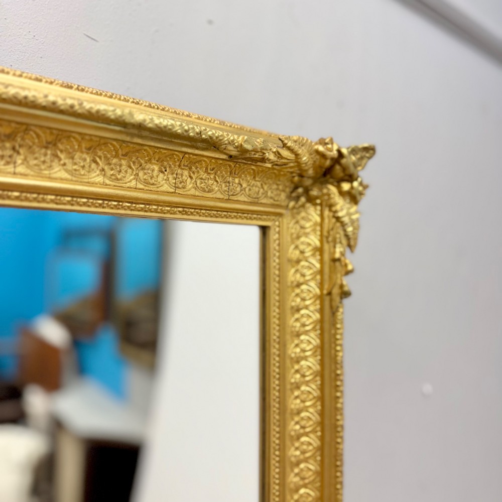 A rectangular nineteenth-century English wall mirror featuring a gold gilded frame with carved foliage corner embellishments and beaded moulding. View II