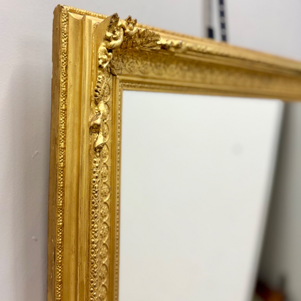 A rectangular nineteenth-century English wall mirror featuring a gold gilded frame with carved foliage corner embellishments and beaded moulding. View V