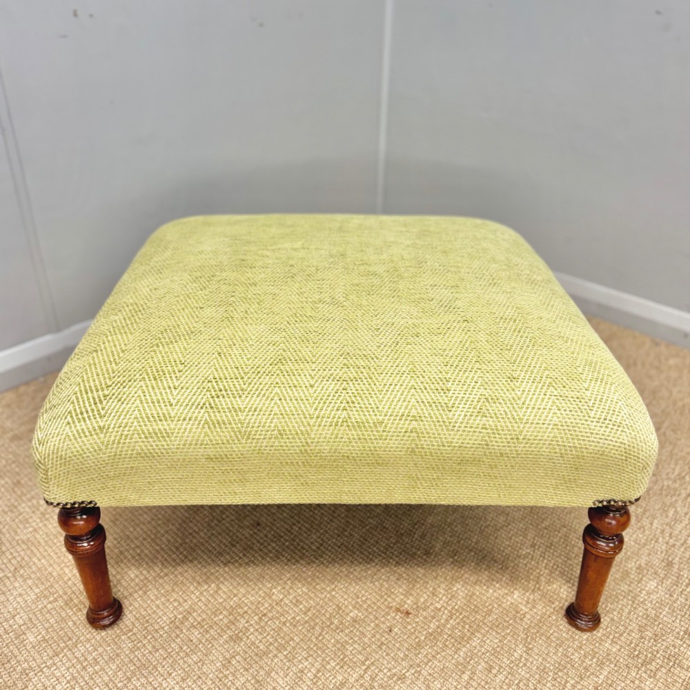 A square footstool upholstered in light green herringbone fabric featuring brass stud trim and four dark turned wooden legs. View III