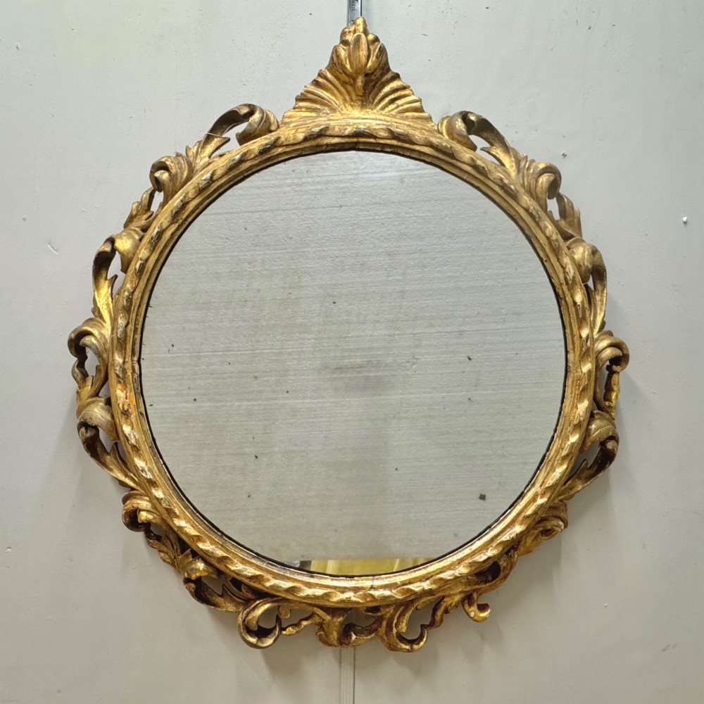 A circular giltwood wall mirror framed in carved acanthus leaves and topped with a shell crest.