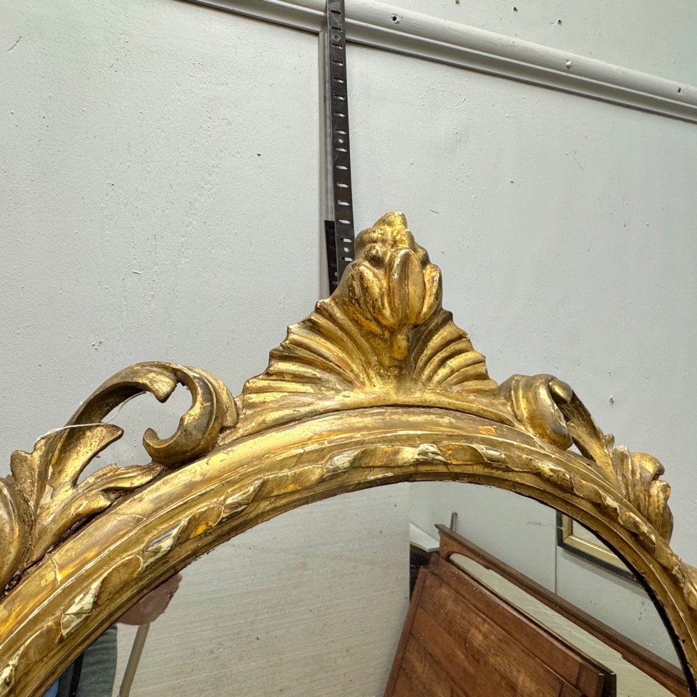 A circular giltwood wall mirror framed in carved acanthus leaves and topped with a shell crest. View II