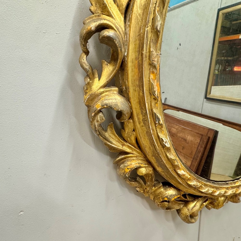 A circular giltwood wall mirror framed in carved acanthus leaves and topped with a shell crest. View III
