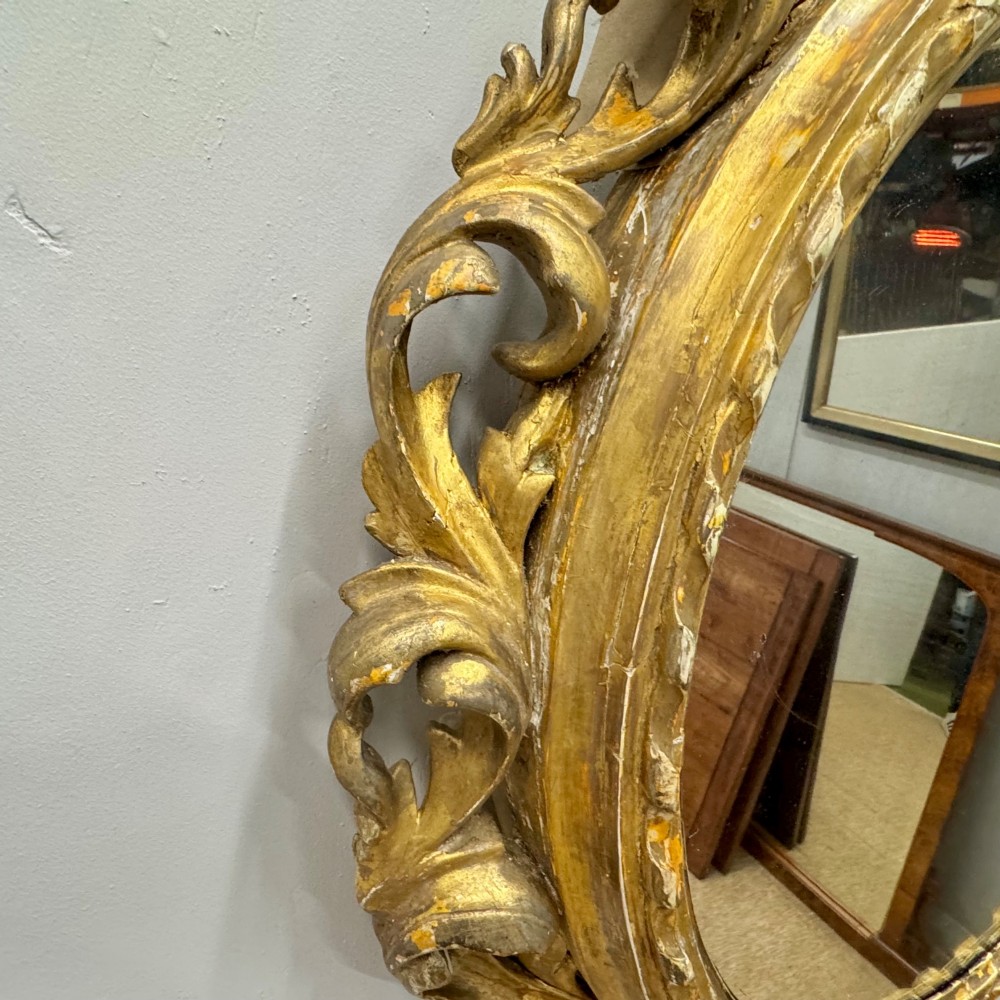 A circular giltwood wall mirror framed in carved acanthus leaves and topped with a shell crest. View V