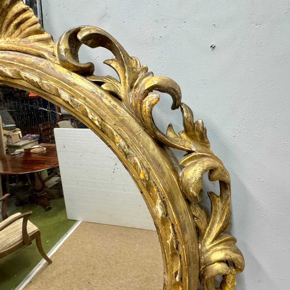A circular giltwood wall mirror framed in carved acanthus leaves and topped with a shell crest. View VII