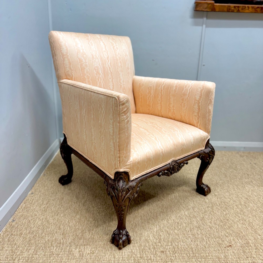 A Georgian armchair upholstered in pale peach damask fabric featuring carved mahogany hipped cabriole legs with claw and ball feet.