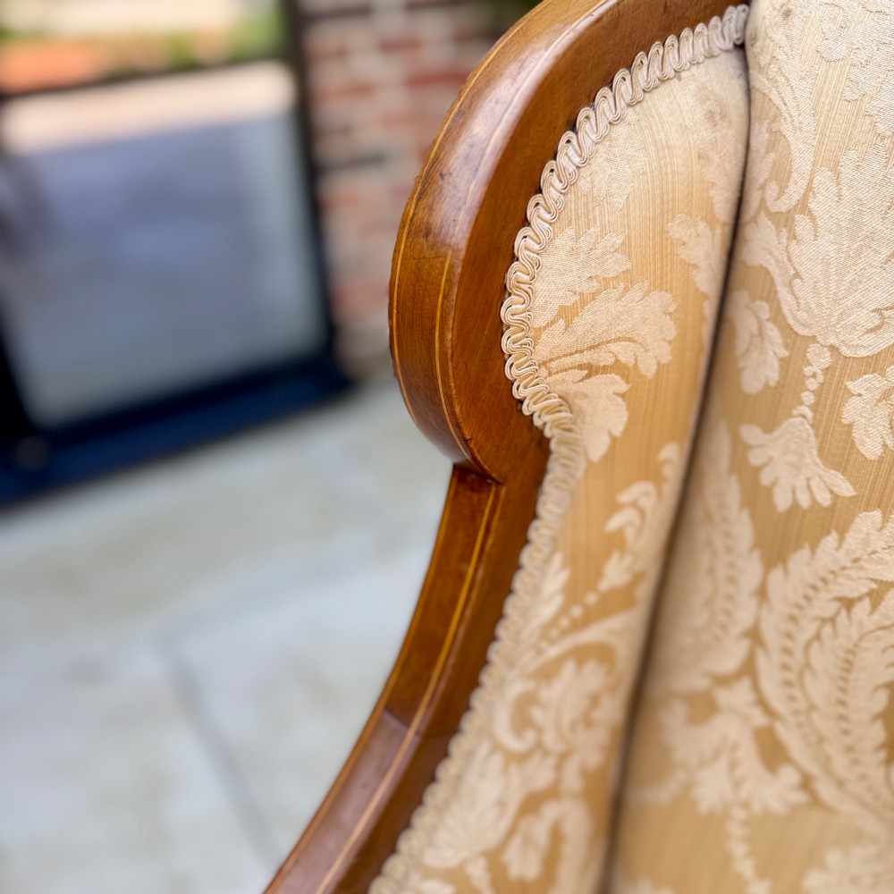 An Edwardian inlaid mahogany wing armchair upholstered in gold patterned damask with turned front legs on brass castors. View III