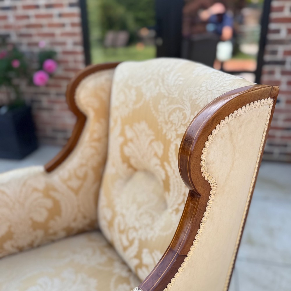 An Edwardian inlaid mahogany wing armchair upholstered in gold patterned damask with turned front legs on brass castors. View IV