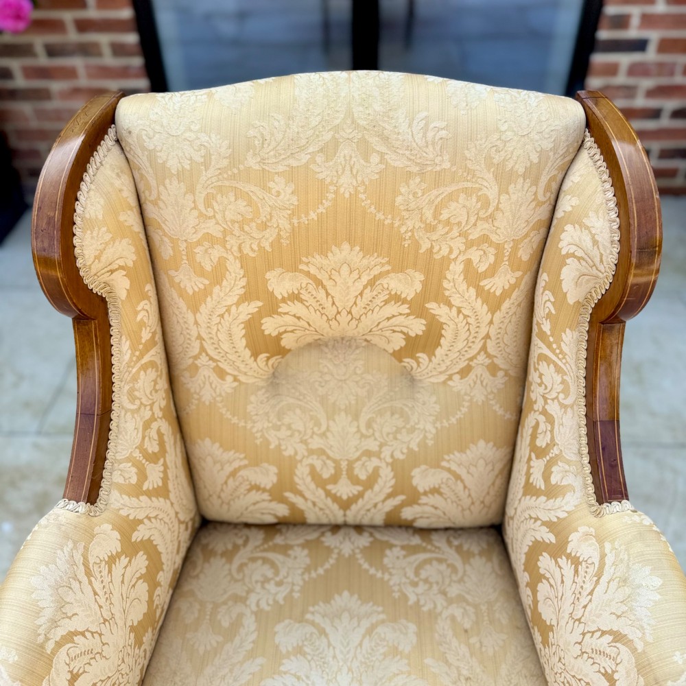 An Edwardian inlaid mahogany wing armchair upholstered in gold patterned damask with turned front legs on brass castors. View V