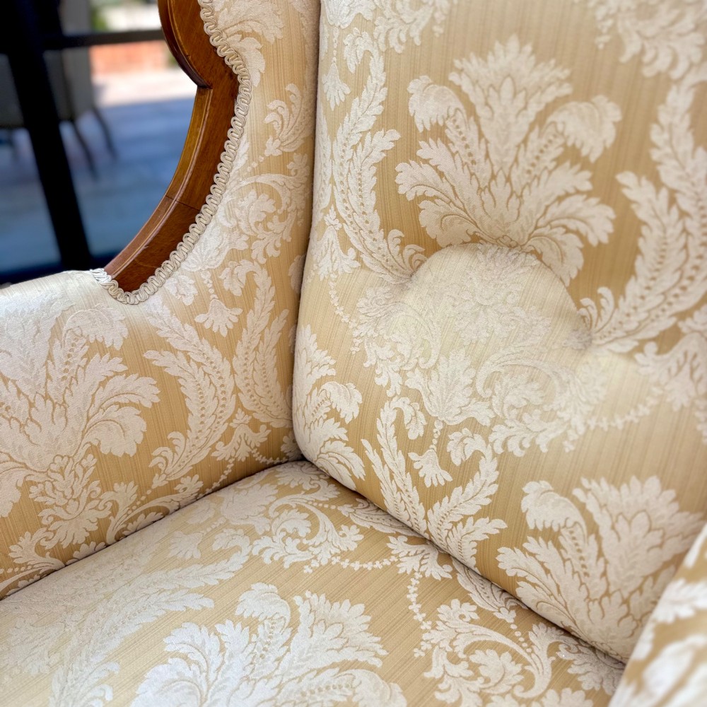 An Edwardian inlaid mahogany wing armchair upholstered in gold patterned damask with turned front legs on brass castors. View VII