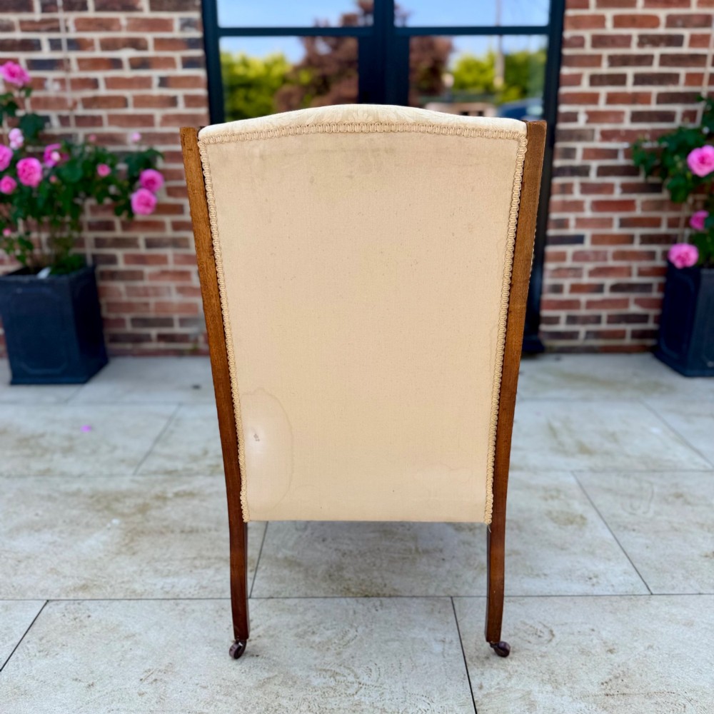 An Edwardian inlaid mahogany wing armchair upholstered in gold patterned damask with turned front legs on brass castors. View VIII