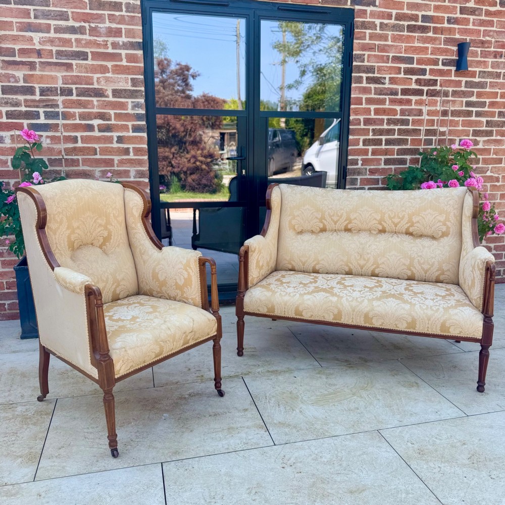 An Edwardian inlaid mahogany wing armchair upholstered in gold patterned damask with turned front legs on brass castors. View IX