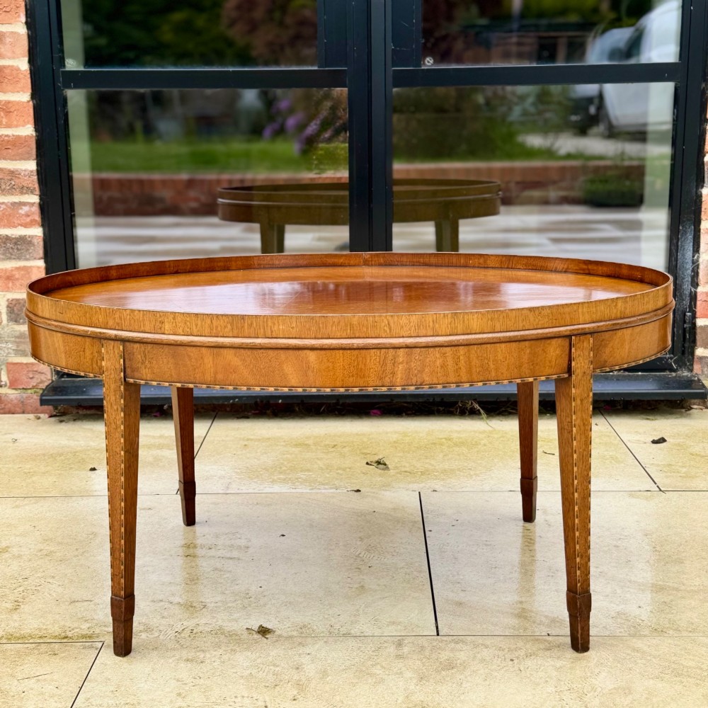 An oval timber coffee table featuring chevron marquetry inlay, a raised rim gallery, and four tapered legs.