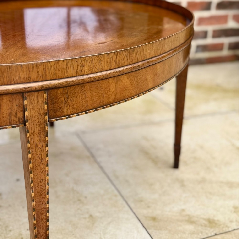 An oval timber coffee table featuring chevron marquetry inlay, a raised rim gallery, and four tapered legs. View IV