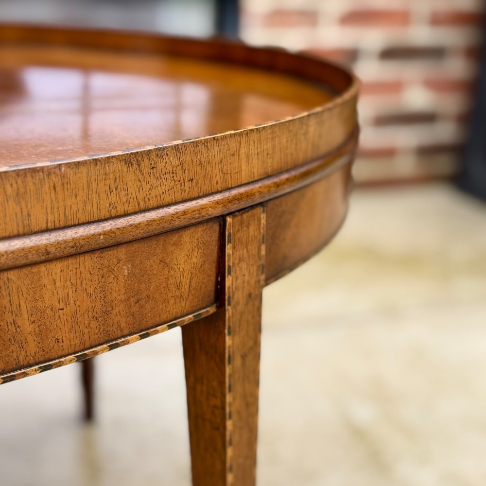 An oval timber coffee table featuring chevron marquetry inlay, a raised rim gallery, and four tapered legs. View V