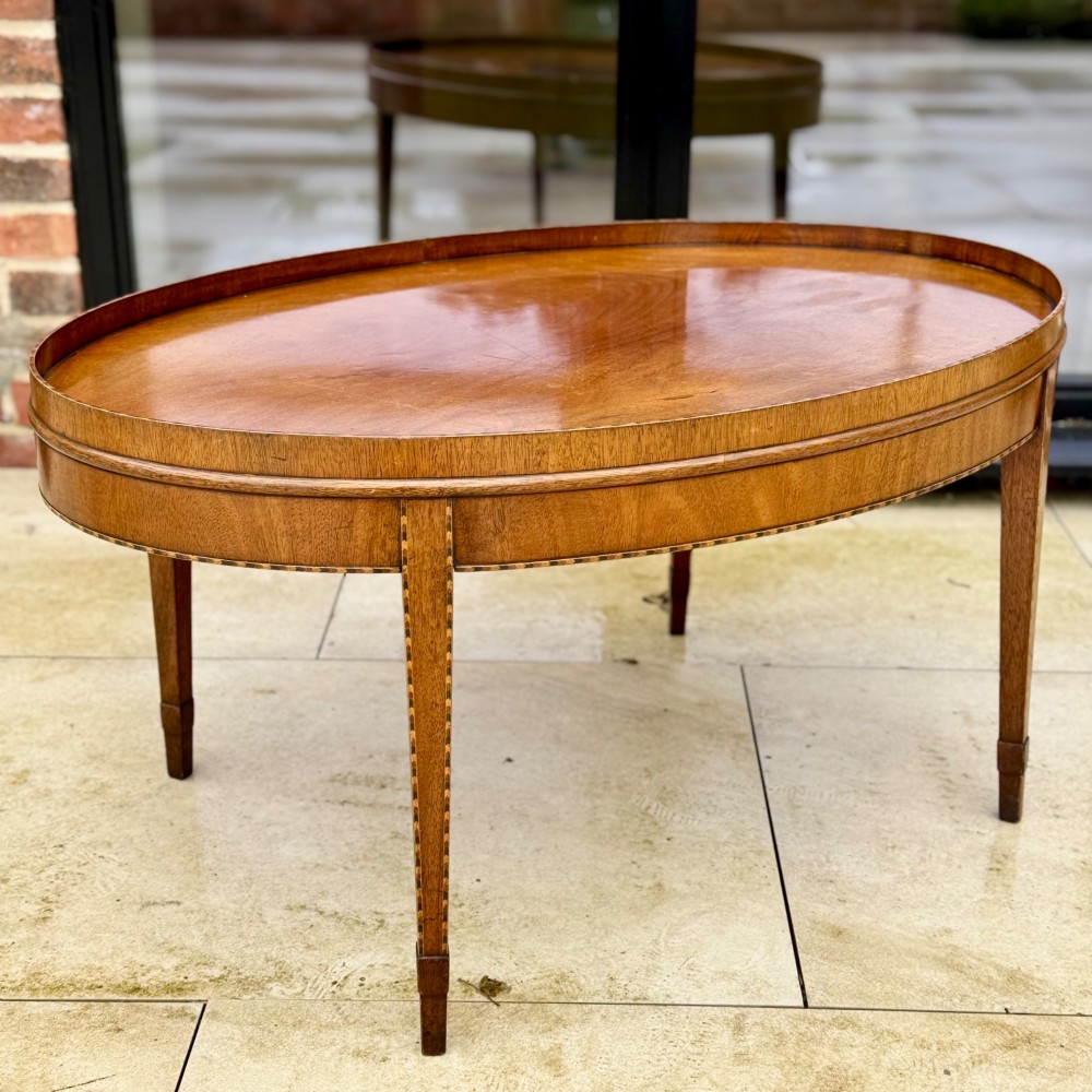 An oval timber coffee table featuring chevron marquetry inlay, a raised rim gallery, and four tapered legs. View VI
