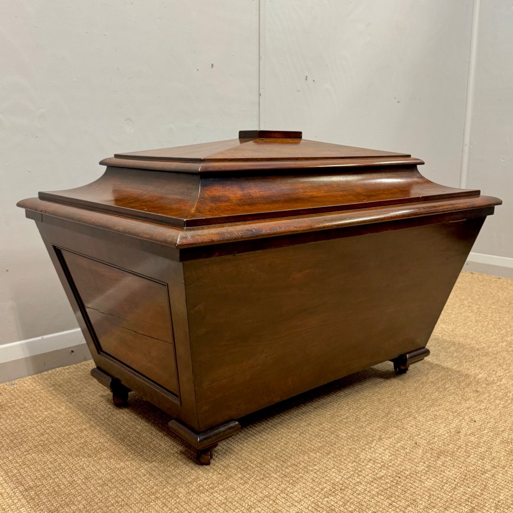 A late Georgian mahogany cellarette displaying a tapered sarcophagus shape with a stepped lid and flame mahogany panels. View II