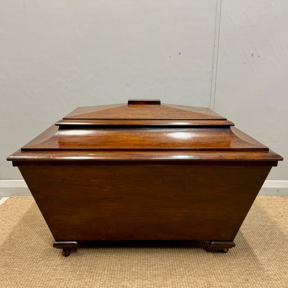 A late Georgian mahogany cellarette displaying a tapered sarcophagus shape with a stepped lid and flame mahogany panels. View IV