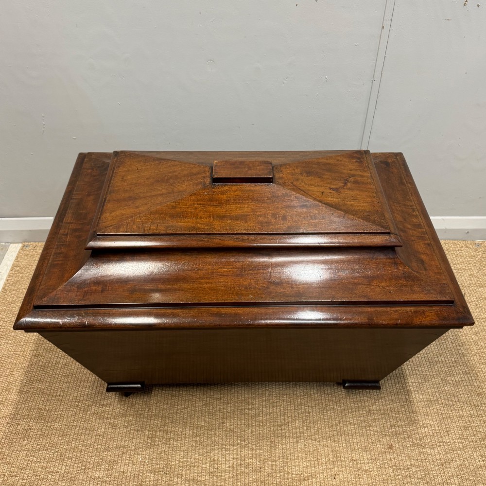 A late Georgian mahogany cellarette displaying a tapered sarcophagus shape with a stepped lid and flame mahogany panels. View V