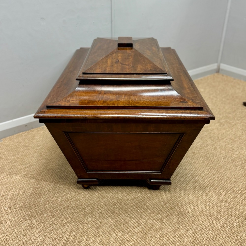 A late Georgian mahogany cellarette displaying a tapered sarcophagus shape with a stepped lid and flame mahogany panels. View IX