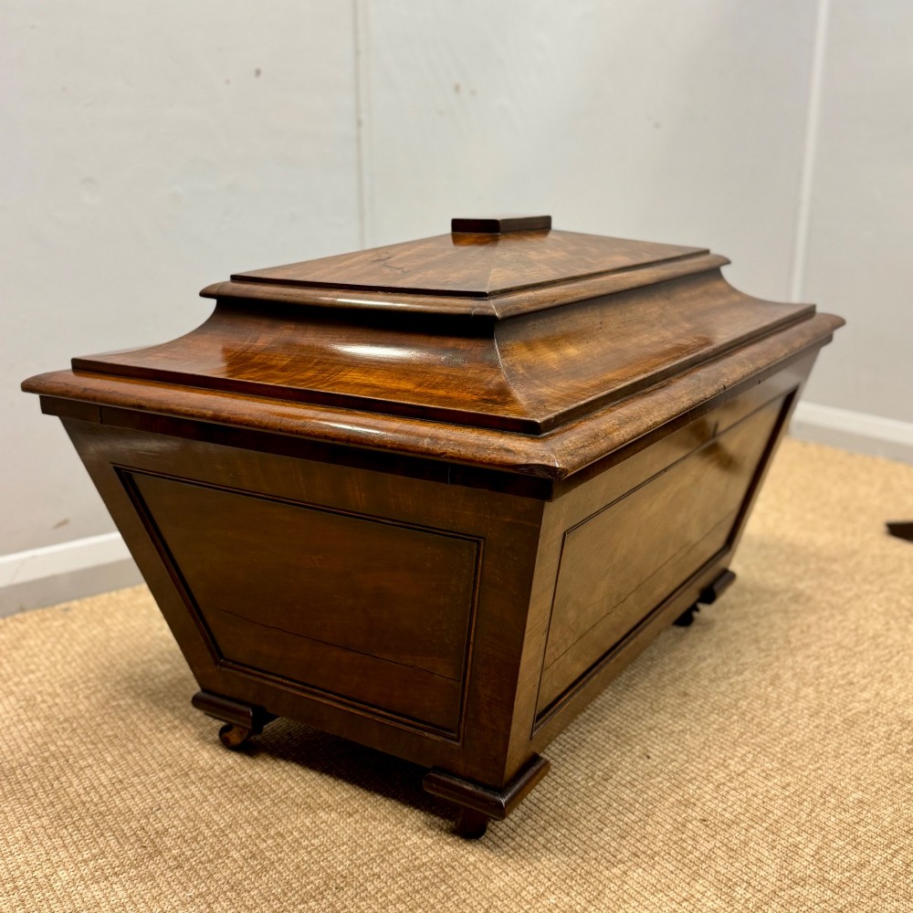 A late Georgian mahogany cellarette displaying a tapered sarcophagus shape with a stepped lid and flame mahogany panels. View X