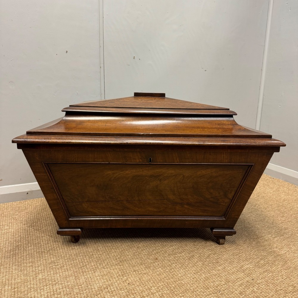 A late Georgian mahogany cellarette displaying a tapered sarcophagus shape with a stepped lid and flame mahogany panels.