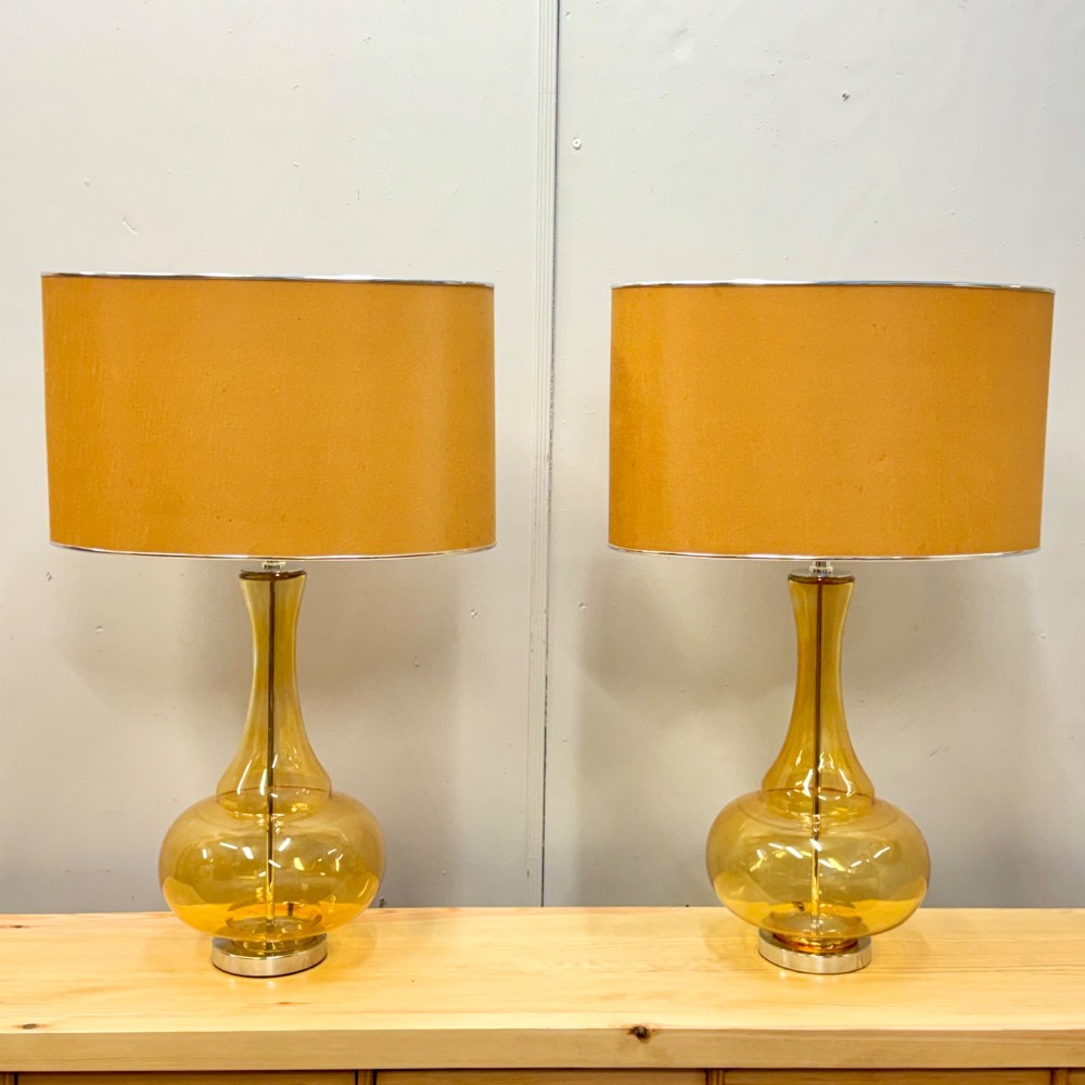 A pair of mid-century amber blown glass table lamps featuring slender necks, bulbous bases, and matching ochre drum shades.