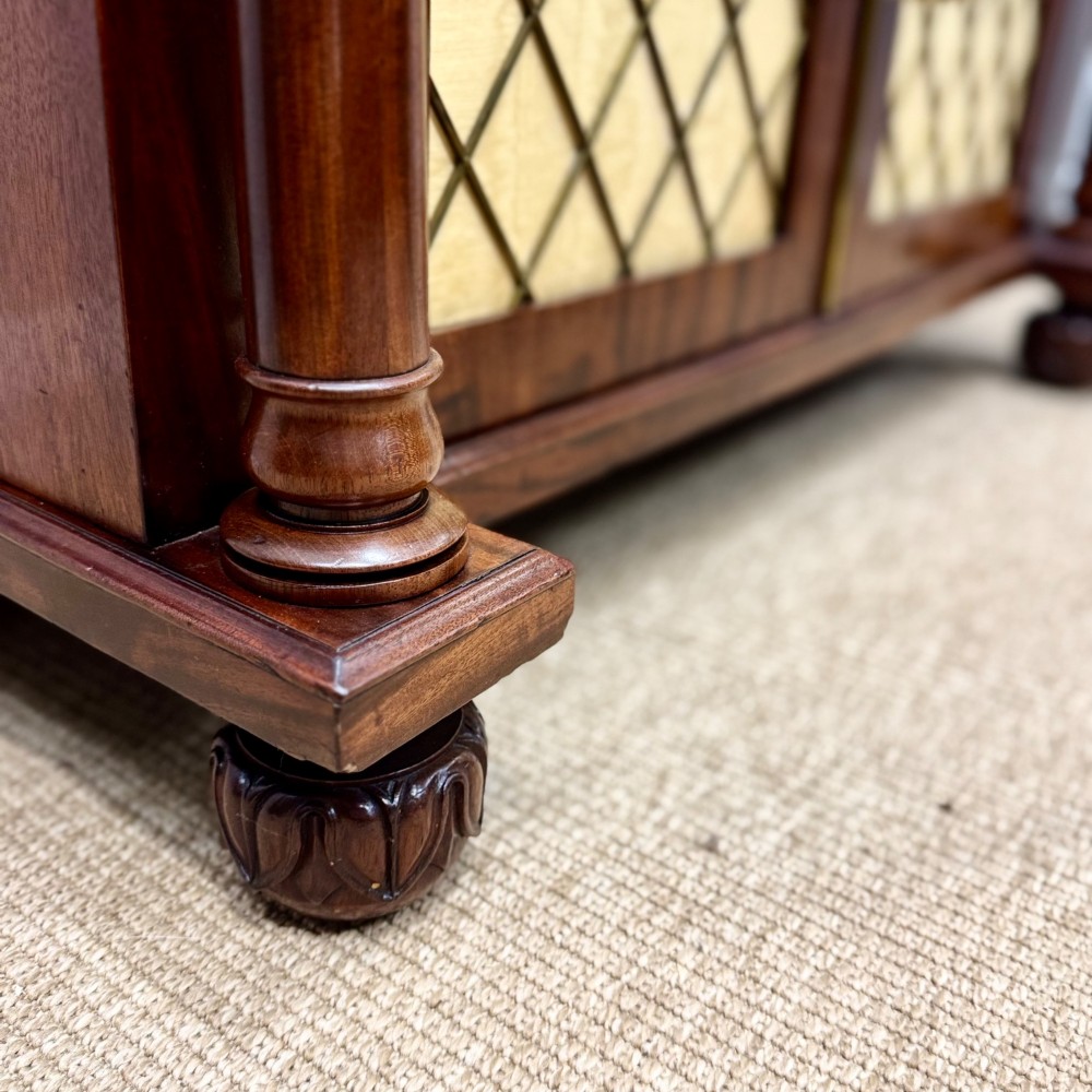 A Regency flame mahogany chiffonier cabinet featuring an upper shelf on turned columns above double doors with brass wire grilles. View V