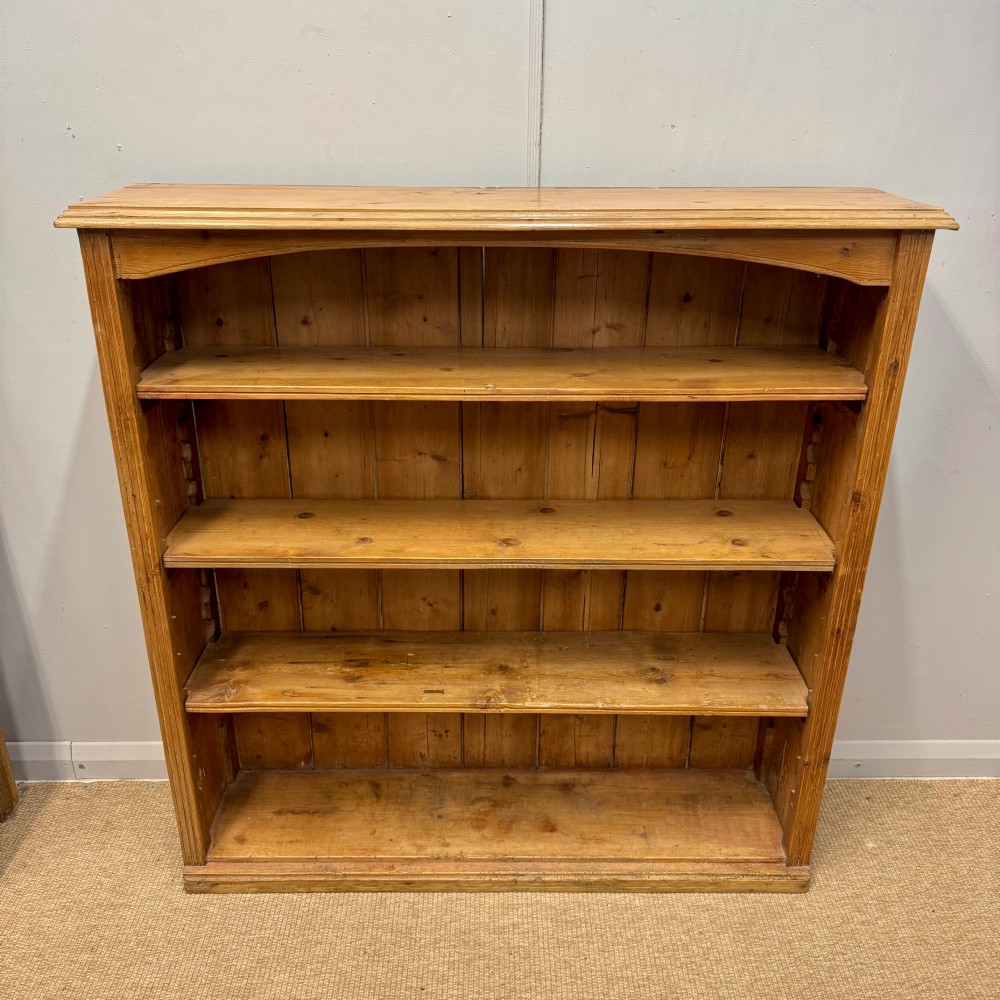 A Victorian open pine bookcase featuring four adjustable shelves, a soft curved top arch, and vertical planked backboards.