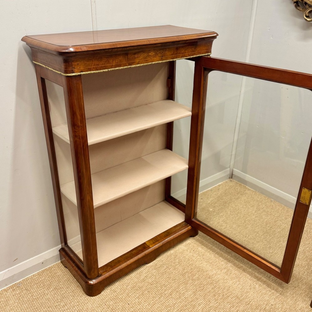 Victorian walnut pier cabinet featuring a single glazed door, floral marquetry inlay on the frieze, brass rim trim, and a three-tier fabric-lined interior. View V