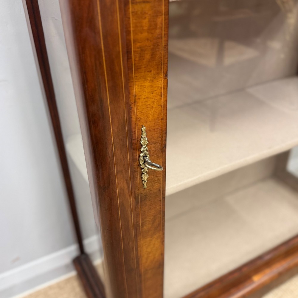 Victorian walnut pier cabinet featuring a single glazed door, floral marquetry inlay on the frieze, brass rim trim, and a three-tier fabric-lined interior. View VI
