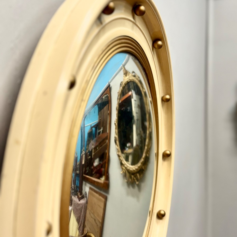 A circular convex wall mirror featuring a cream painted frame embellished with gold spherical studs and a reeded gold inner border. View II