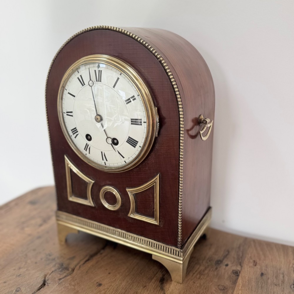 An arched antique French mahogany mantel clock featuring a white face with Roman numerals, decorative brass trim, and a stepped brass base. View II