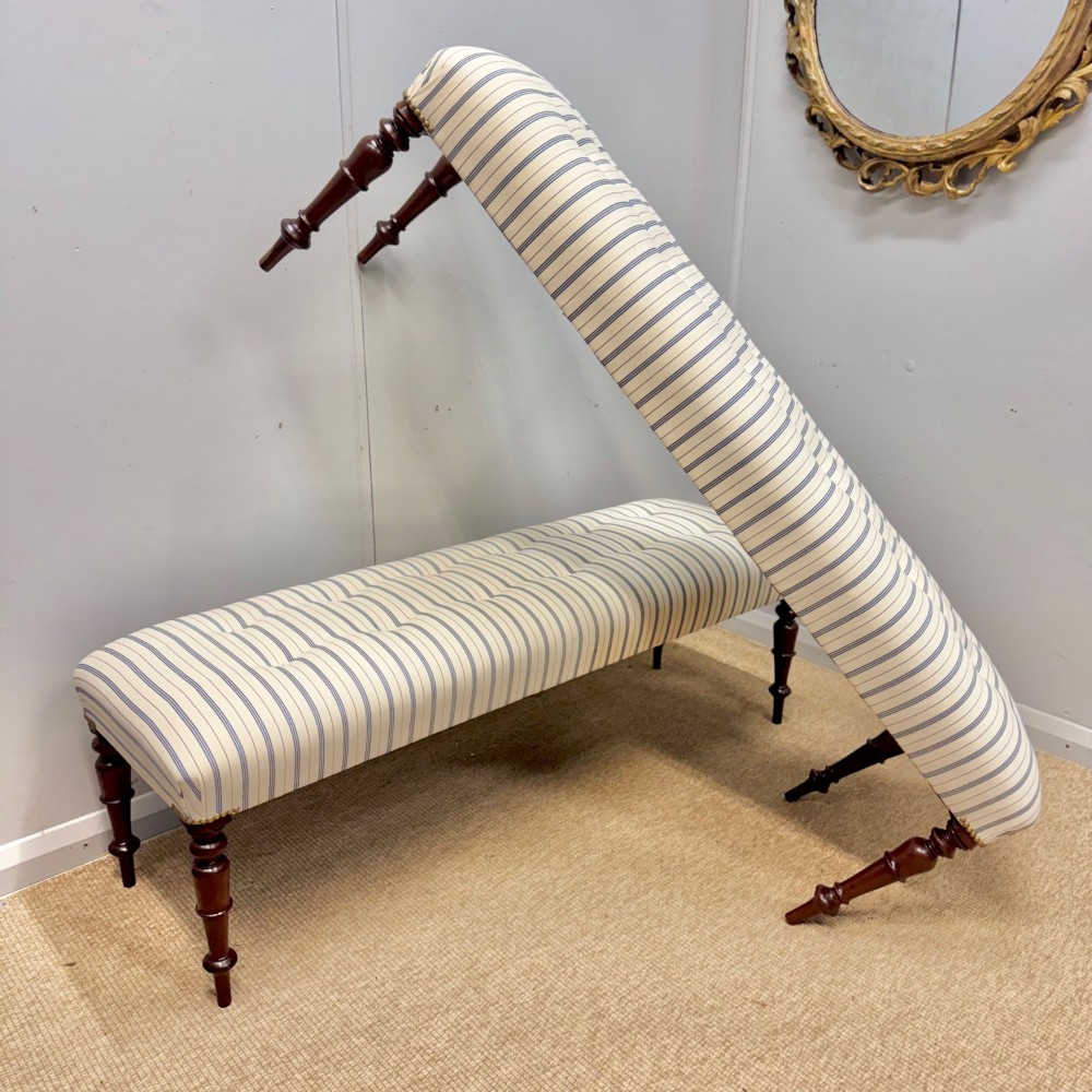 A pair of five-foot long upholstered stools with cream and blue striped buttoned ticking fabric set upon dark turned mahogany legs with brass studs. View II