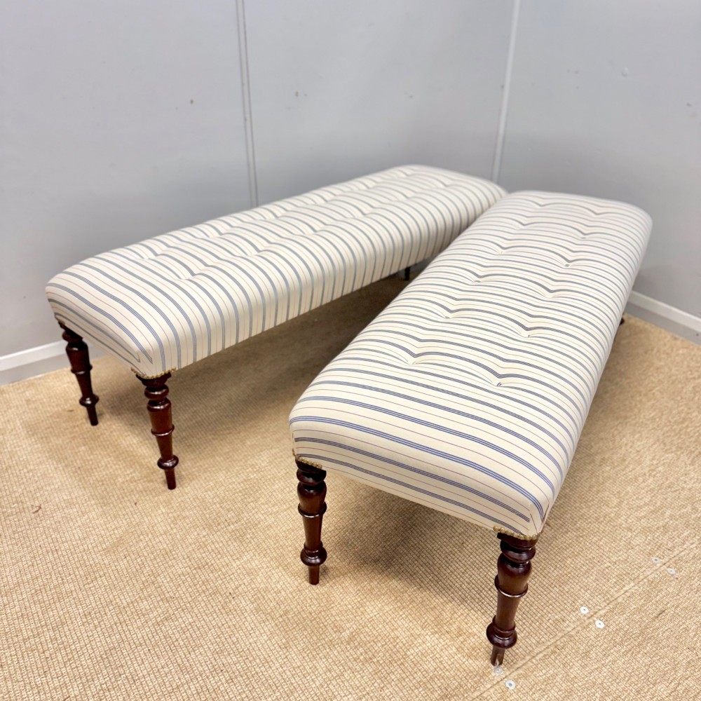 A pair of five-foot long upholstered stools with cream and blue striped buttoned ticking fabric set upon dark turned mahogany legs with brass studs. View III