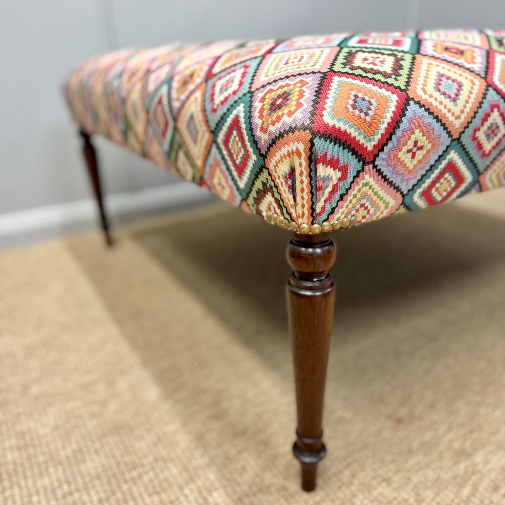 A large rectangular footstool upholstered in a vibrant geometric diamond pattern featuring turned mahogany legs. View II