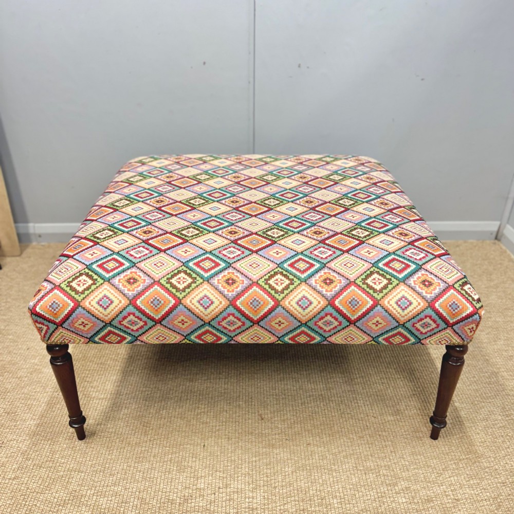 A large rectangular footstool upholstered in a vibrant geometric diamond pattern featuring turned mahogany legs. View VI