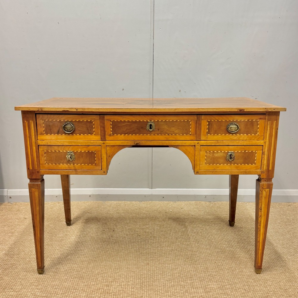 An early nineteenth-century freestanding wood writing desk featuring intricate marquetry inlays, five drawers with brass handles, an arched kneehole, and square tapered legs.