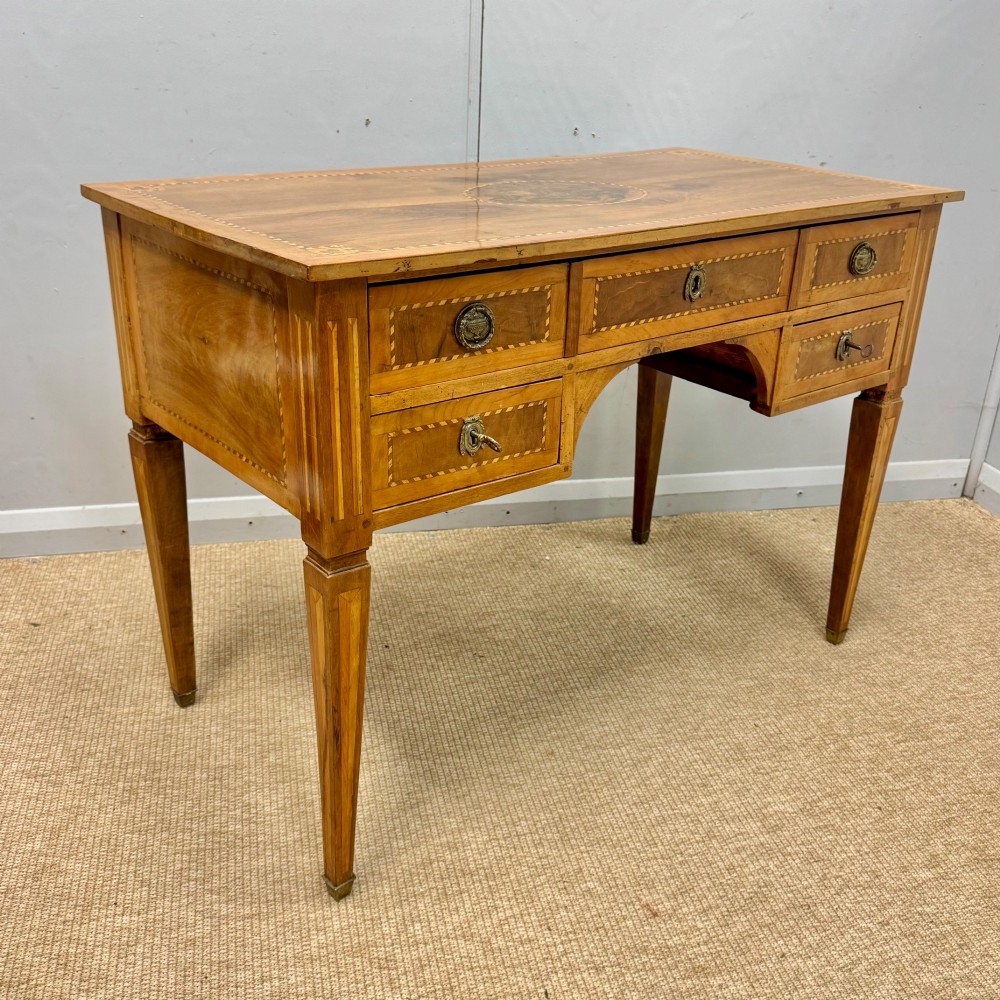 An early nineteenth-century freestanding wood writing desk featuring intricate marquetry inlays, five drawers with brass handles, an arched kneehole, and square tapered legs. View II