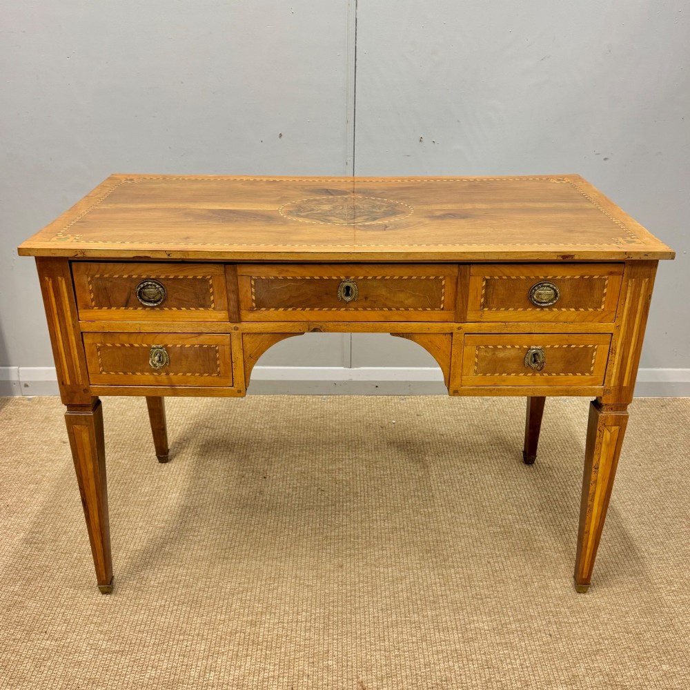 An early nineteenth-century freestanding wood writing desk featuring intricate marquetry inlays, five drawers with brass handles, an arched kneehole, and square tapered legs. View III