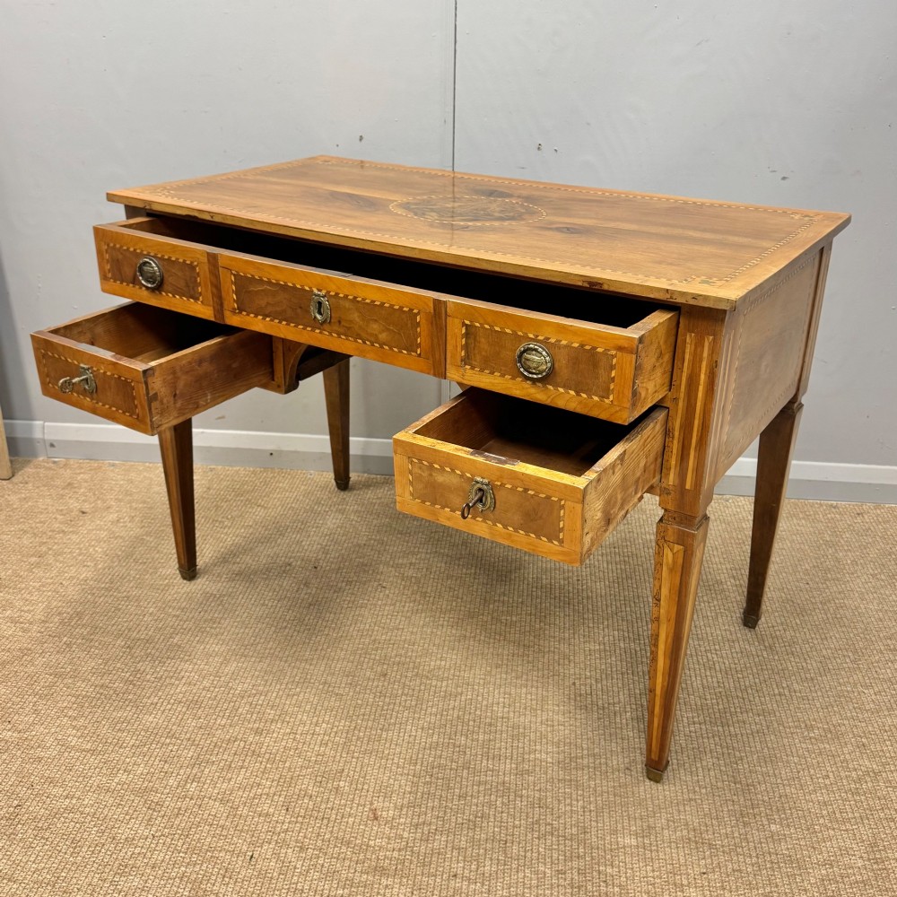 An early nineteenth-century freestanding wood writing desk featuring intricate marquetry inlays, five drawers with brass handles, an arched kneehole, and square tapered legs. View IV