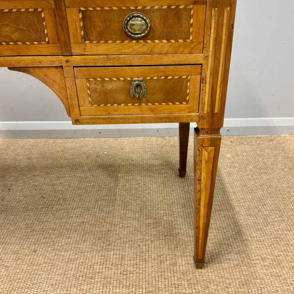 An early nineteenth-century freestanding wood writing desk featuring intricate marquetry inlays, five drawers with brass handles, an arched kneehole, and square tapered legs. View VI
